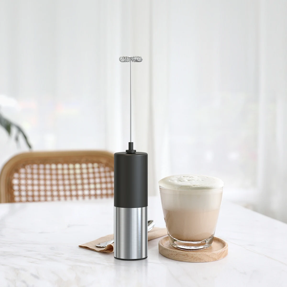 Black and stainless steel milk frother on a marble counter next to a glass of cappuccino